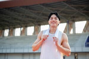 Asian man in white tank top standing and holding a towel on shoulder, taking a rest after running. photo