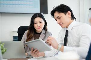 Male office worker is pointing stylus at tablet screen showing business data to his female coworker. photo