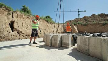 Construction Workers Direct Heavy Concrete Blocks with Crane on Excavated Site under Clear Blue Sky video