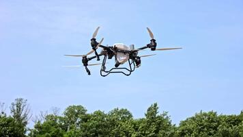 Modern agricultural drone flying in clear blue sky above treetops, demonstrating aerial precision farming technology for smart crop management in rural video