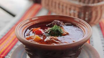 Traditional Hungarian bograch soup with meat, vegetables, and spices served in clay pot, authentic hearty dish from Zakarpattia region on ethnic tablecloth in video