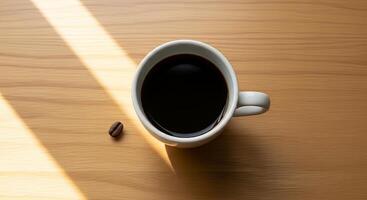 A cup of dark coffee sits on a wooden table in sunlight, a single coffee bean rests nearby photo