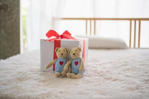 Two teddy bears sitting on a bed with a gift photo