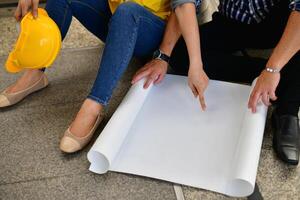 A man and woman sitting on the floor with a blueprint photo