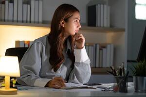 Late Night Work. Focused woman analyzing documents at desk in dimly lit office. photo