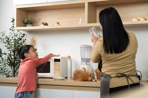 Learning and Helping. Child asking mother for assistance while she prepares a smoothie in the kitchen. photo