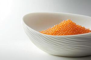 A white bowl filled with orange fish roe. The roe is small, round, and glossy, creating a vibrant contrast against the smooth surface of the bowl. photo