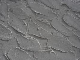 Textured wall surface with rough, uneven plaster finish showing cracks and ridges, creating rugged appearance with shadows highlighting depth and irregularities of material photo