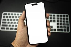 Hand Holding Blank Smartphone Over Keyboard. Perfect for showcasing mobile apps or web designs against a blurred keyboard background. photo