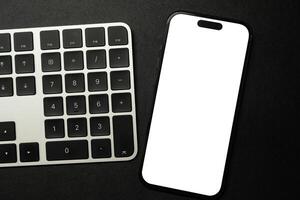 A modern smartphone with a blank white screen rests on a white and black computer keyboard, ideal for showcasing digital content or technology concepts. photo