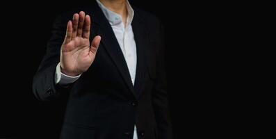 Businessman shows a stop gesture while standing on a black background. photo