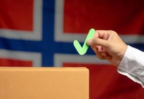 Hand holding a green check mark symbol overhead the voting box at place election with the Norway flag background photo