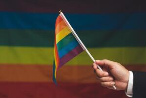Rainbow flag in hand against a rainbow flag background photo
