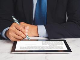 Signature electronic. Businessman signing a digital contract or agreement on a tablet while sitting in the office photo