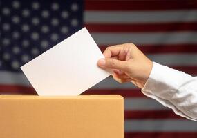 Close-up of a hand voter holding ballot paper putting into the voting box at place election against the American flag background photo