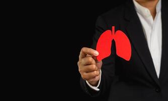 Man in a suit holding a lung shape symbol while standing on a black background photo
