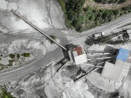 Aerial drone view of industrial stone crushing plant with conveyor belts and truck at limestone processing facility surrounded by forest, showing heavy equipment infrastructure and quarry operations. photo