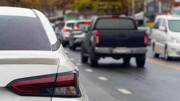Rear side of white car stop on the wet road. Traffic on the road in rainy time. on the body of car wet drop of rain. Traffic jam in the city after rainy time. Side of road with many cars. photo