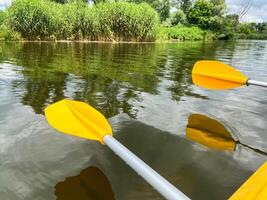 Kayaking on the river with bright yellow paddles and lush green riverbank photo