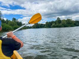Kayaker paddling on lake with lush green trees and cloudy sky photo
