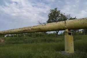Gas pipe goes across the field. Huge pipe in diameter yellow color against the background of rural landscape, green grass in the field. Concept of ecological safety and infrastructure. photo