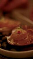Close-up of scallops garnished with herbs and sauce, under warm, ambient lighting, with a hand adjusting the presentation video