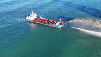 Aerial view of a dredging vessel pumping sand in clear ocean waters under bright sunlight video