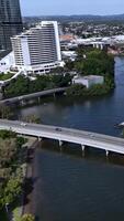 Aerial footage captures a bridge over a river, adjacent to urban buildings and lush greenery, under clear daylight video