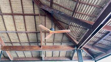 A wooden ceiling fan rotates under a rustic, open-air roof in Phuket, Thailand. Natural lighting highlights the wooden beams and fan blades video