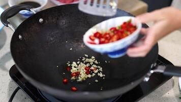 Close-up of hands adding chilli and garlic to a hot wok. Bright kitchen lighting, dynamic movement, culinary focus video