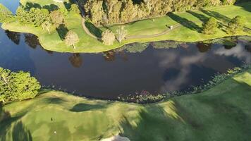 Drone footage captures a serene golf course with lush greenery and a reflective lake under bright sunlight video
