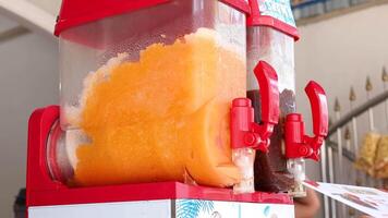 A vibrant orange slushy machine operates in a bustling Phuket market, with bright lighting and dynamic camera angles capturing the scene video