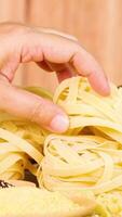 A hand selects tagliatelle pasta from a neatly arranged pile on a wooden surface, under warm lighting video