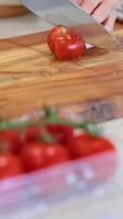 A person slices a tomato on a wooden cutting board in a well-lit kitchen setting video