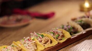 A variety of tacos arranged on a wooden table, illuminated by warm candlelight, creating a cozy dining atmosphere video