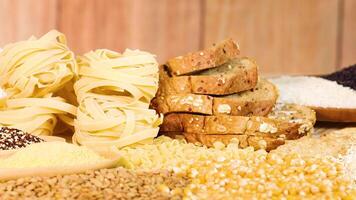 A hand organizes various grains and breads on a wooden table with warm lighting, emphasizing texture and variety video