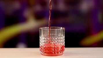 A vibrant Negroni cocktail is poured into a textured crystal glass against a colorful background, highlighting the drink's rich red hue video