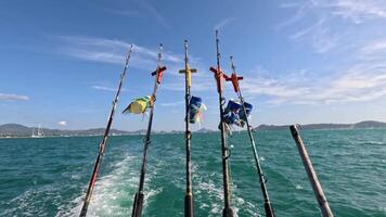 Fishing rods sway on a moving boat under clear skies in Phuket, Thailand. Vibrant ocean and flags create a dynamic scene video