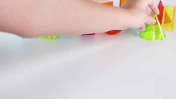 Hands manipulate vibrant 3D geometric shapes on a white surface, demonstrating movement and interaction in a colorful setting video