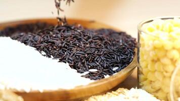 Riceberry and white rice in a wooden bowl with corn kernels. Dynamic pouring action captured in warm lighting video