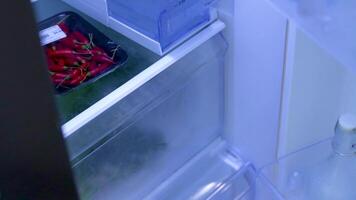 A person opens a refrigerator, selecting fresh vegetables under bright lighting in a kitchen setting video