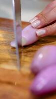 Close-up of hands slicing shallots on a wooden board with a sharp knife under bright lighting video