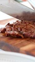 A chef slices a grilled beef steak on a wooden board. Natural lighting enhances the texture and color video