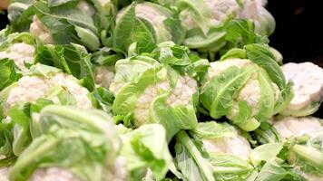 Close-up view of fresh cauliflower heads in a well-lit supermarket setting, highlighting texture and vibrant green leaves video