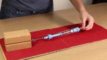 A hand pulls a wooden block across sandpaper using a spring scale, demonstrating friction and force measurement video