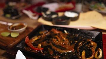 Beef fajitas with peppers and onions on a hot plate, surrounded by tortillas and sauces, in a warm restaurant setting video