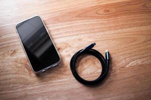Connecting devices phone and charging cable wood surface close-up technology minimalist view photo