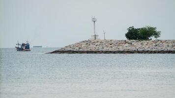 Fishing boat anchored by lighthouse at coastal jetty tranquil waters serene atmosphere wide angle view photo