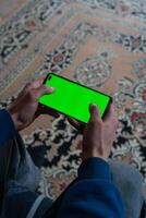 Guy is sitting with a smartphone in his hands with the green screen turned on photo