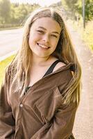 A Smiling Young Woman in Nature Wearing a Brown Jacket amidst a Beautiful Setting photo
